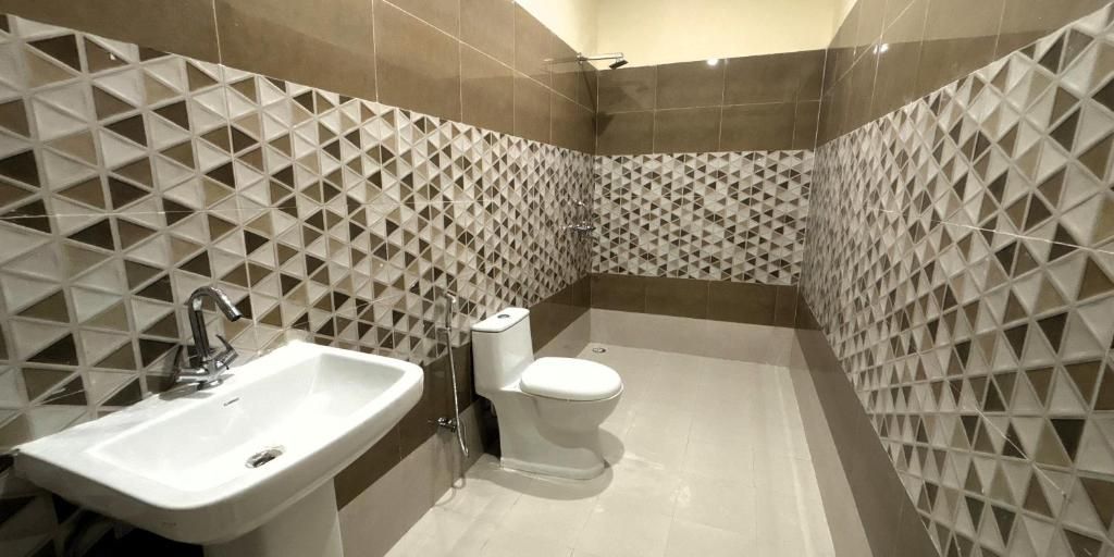A bathroom with a sink, toilet, and shower. The walls have a geometric tile pattern.
