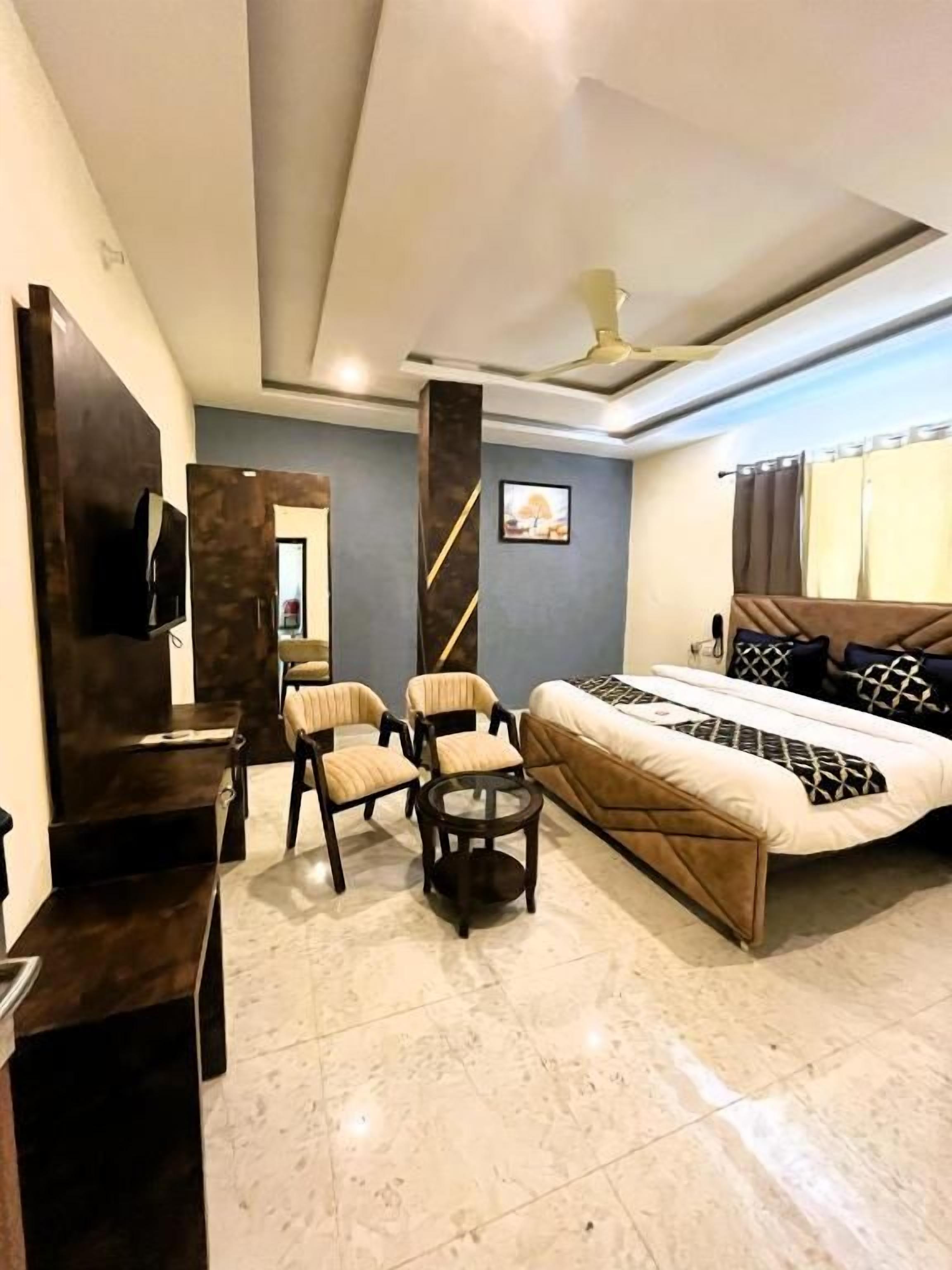 A hotel room with a bed, two armchairs, a small table, a TV, and a ceiling fan.