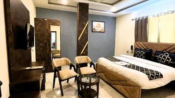 A hotel room with a bed, two armchairs, a small table, a TV, and a ceiling fan.