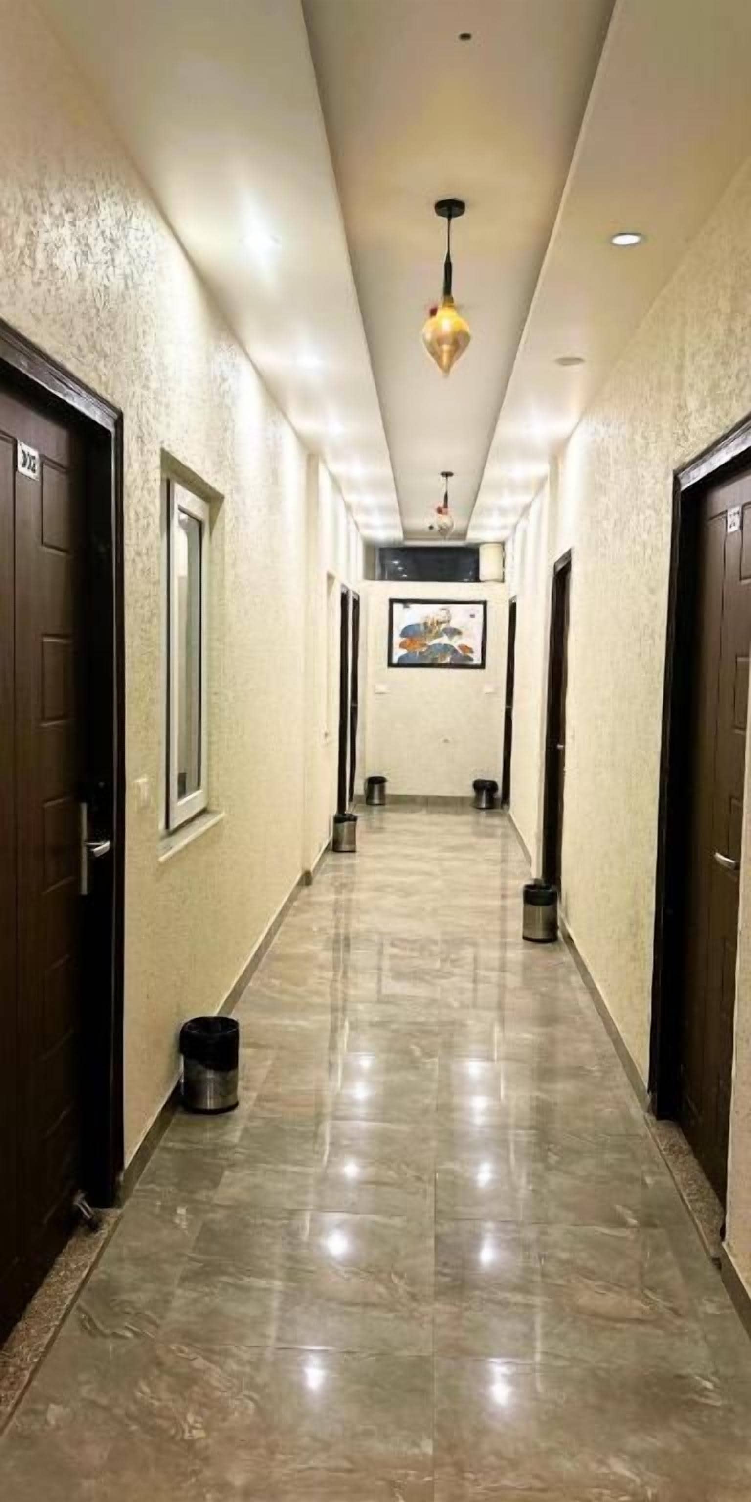 A hotel hallway with a tiled floor, dark wooden doors, and a hanging light fixture.