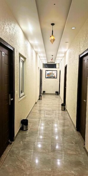 A hotel hallway with a tiled floor, dark wooden doors, and a hanging light fixture. - Grand Parador  (Rishikesh)
