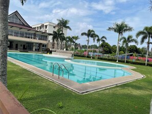 A swimming pool with a clear blue water, surrounded by well-maintained grass and palm trees.