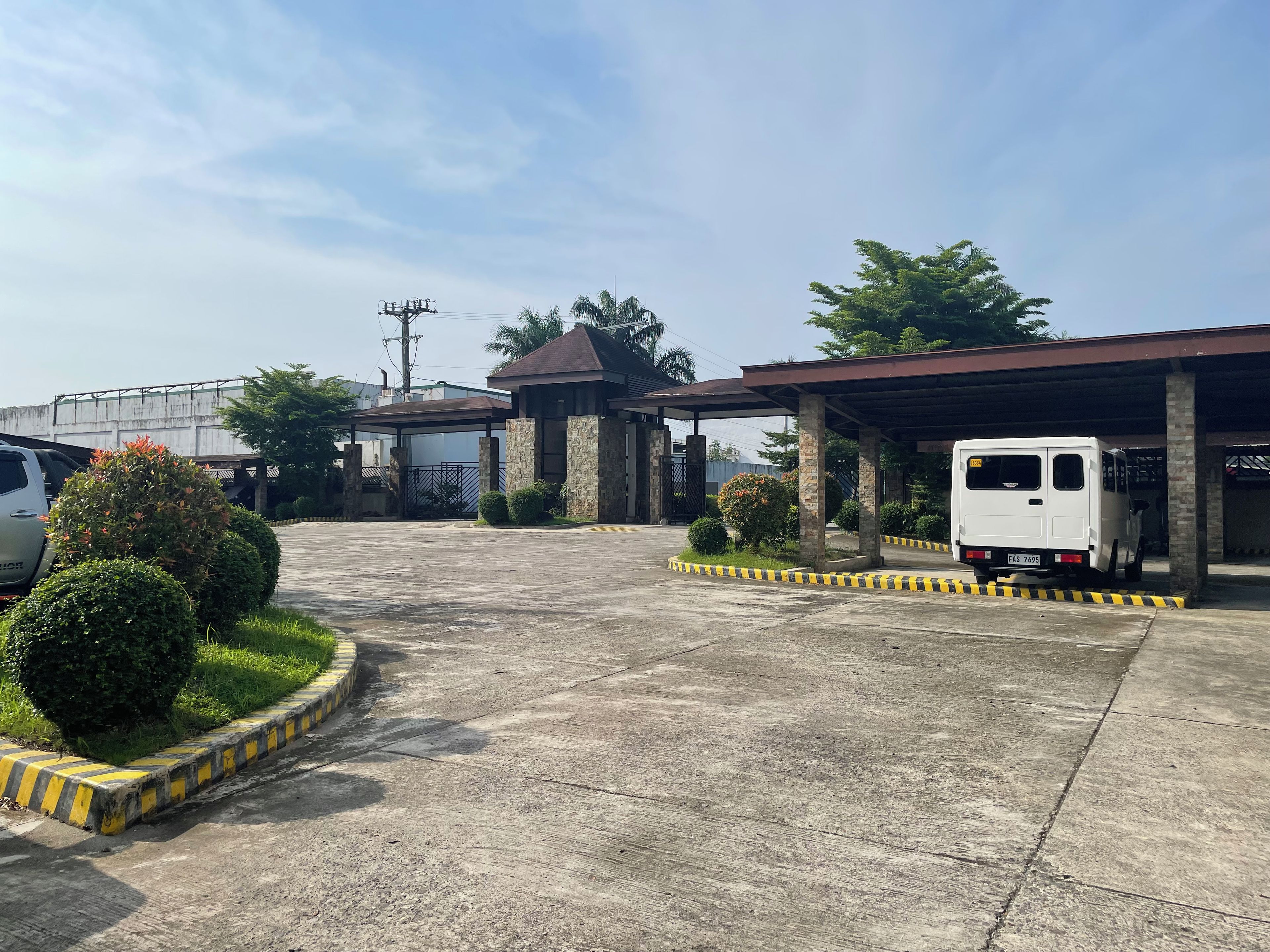 A parking area with a covered structure, a white van, and a gated entrance.