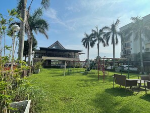A grassy area with a playground, a building with a sloped roof, and palm trees.