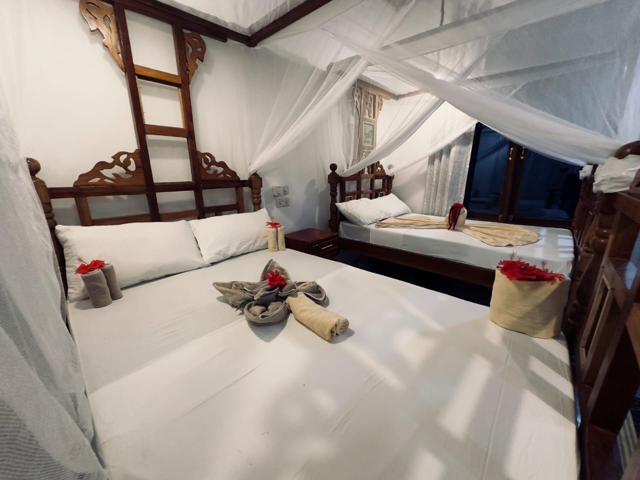 Una habitación de hotel con cama a dosel, otra cama y un cabecero de madera.