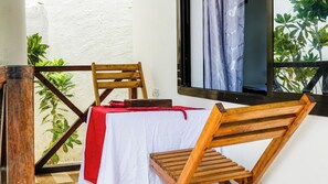A balcony with a wooden chair, a table with a red cloth, and a window with curtains.