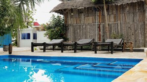A swimming pool with lounge chairs and a thatched-roof structure. - Cheka bungalows (Nungwi)