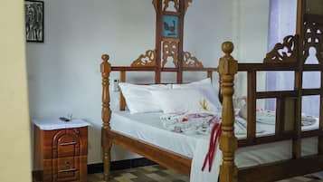 Un lit à baldaquin en bois avec une literie blanche, une table de chevet avec un téléphone et une œuvre d’art accrochée au mur.