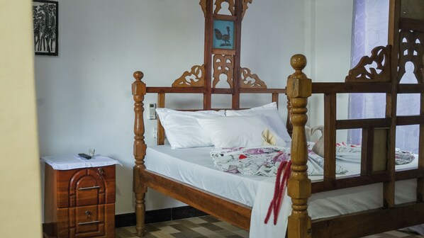 A wooden four-poster bed with white bedding, a bedside table with a telephone, and a wall-mounted artwork.