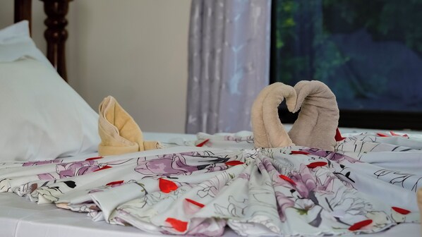 A bed with floral bedding, a heart-shaped towel, and a pillow.
