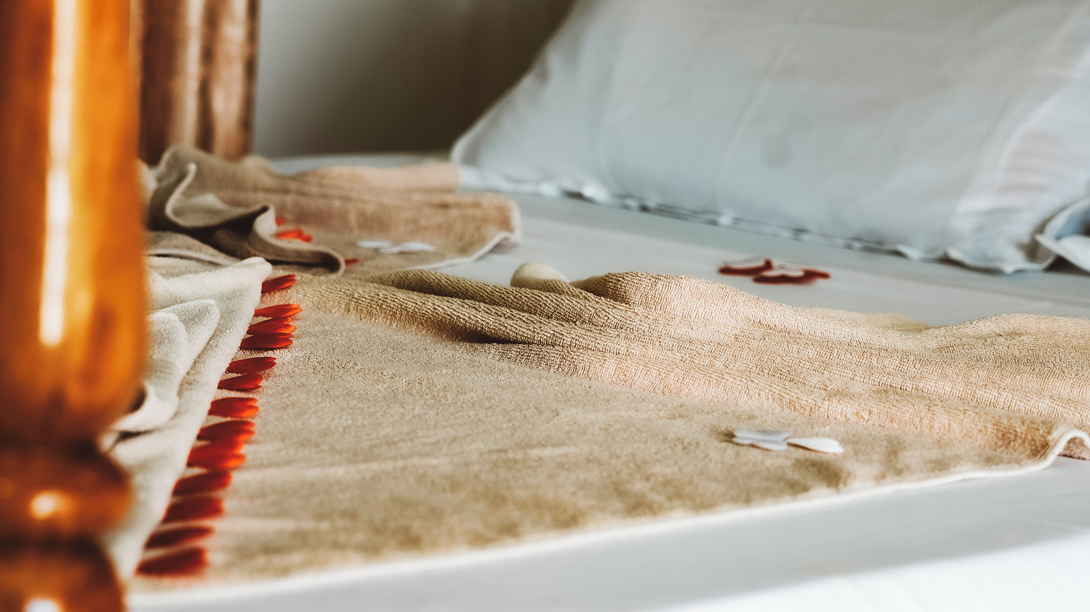 A bed with a beige blanket and red tassels, a white pillow, and a wooden headboard.