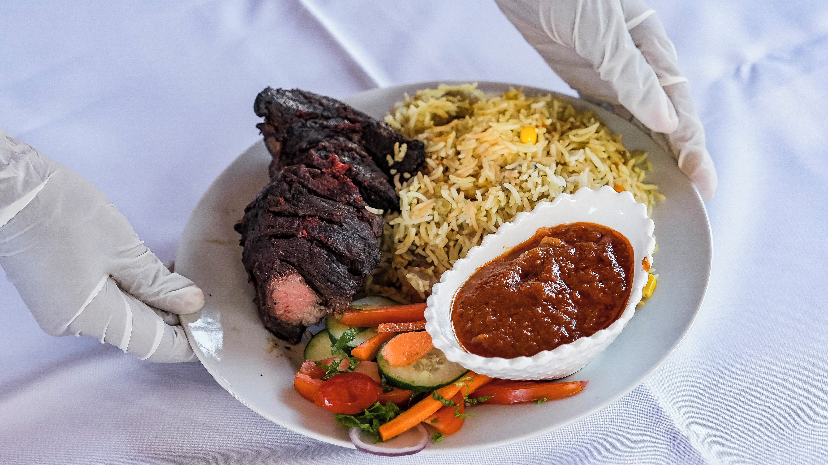 A plate with a meat dish, rice, vegetables, and a sauce.