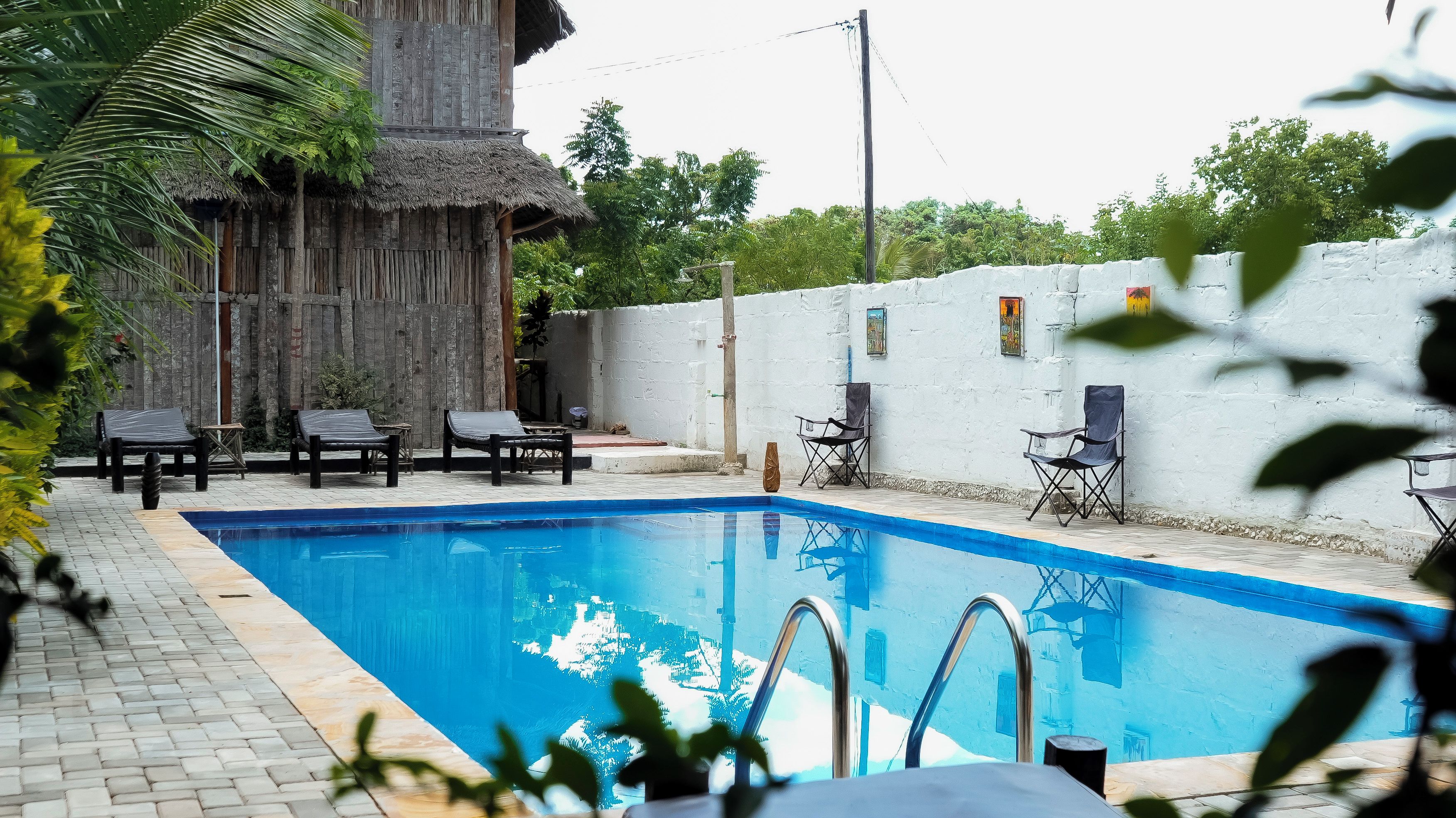 Une piscine avec des chaises longues et une structure surmontée d’un toit de chaume.