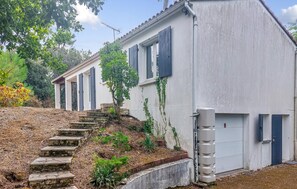 Ein zweistöckiges Gebäude mit einer Steintreppe, die zum Eingang führt, einer Garagentür und einem kleinen Gartenbereich mit Stufen und Pflanzen.