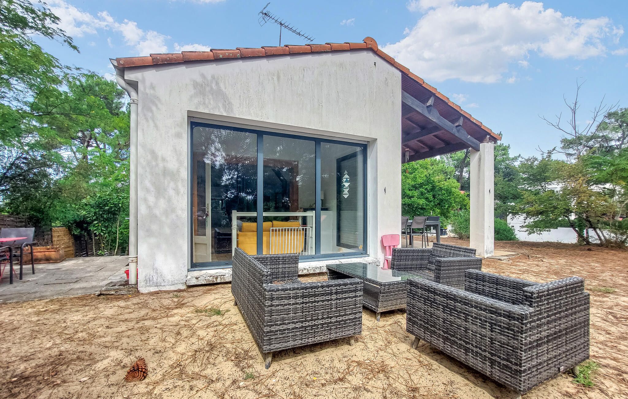 Un espace extérieur moderne, aménagé avec des meubles en osier, une entrée avec une porte en verre et un patio couvert.