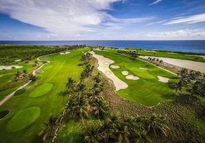 A golf course with multiple bunkers and palm trees, surrounded by ocean views. - Tortuga B50 - 5BR villa with private pool in beach resort (Punta Cana)