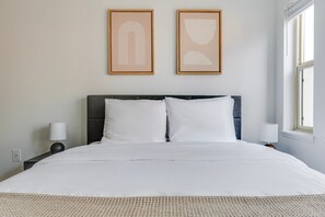 A neatly made bed with white linens, two bedside lamps, and two framed abstract artworks on the wall. - Blueground | Denny Triangle, gym, nr Pike Place (Seattle)