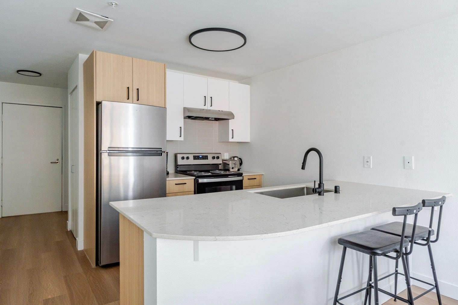 A modern kitchen with a stainless steel refrigerator, a built-in oven, and a large island with a sink.