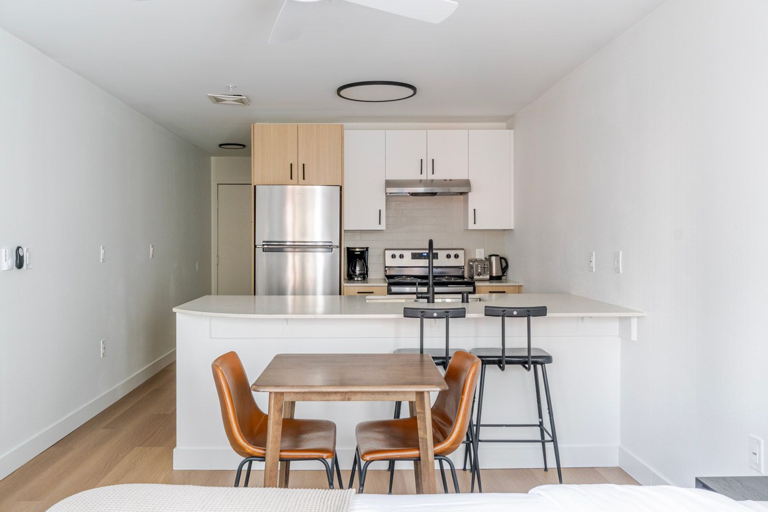 A compact kitchen with a central island, two bar stools, and a dining table with four chairs.