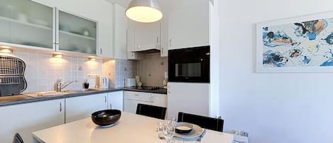 A modern kitchen with white cabinetry, a dining table set for two, and a contemporary art piece on the wall.