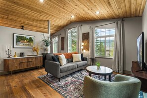 A modern living room with a wooden ceiling, a grey sofa, a round coffee table, and large windows with curtains.