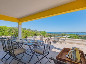 An outdoor dining area with a table set for four, surrounded by chairs, overlooking a scenic view of the sea and greenery. - GRIMAUD VILLA  WITH AN AMAZING SEAVIEW AND SWIMMING POOL (GRIMAUD)