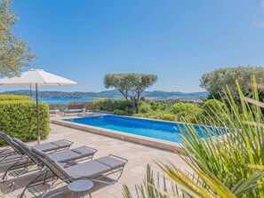 A swimming pool with lounge chairs and a table, surrounded by greenery and a view of the sea. - GRIMAUD VILLA  WITH AN AMAZING SEAVIEW AND SWIMMING POOL (GRIMAUD)