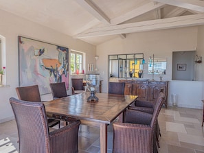 A dining area with a wooden table and wicker chairs, a large abstract painting on the wall, and a kitchen with glass cabinets. - GRIMAUD VILLA  WITH AN AMAZING SEAVIEW AND SWIMMING POOL (GRIMAUD)