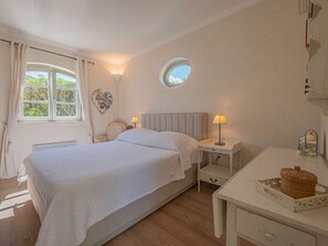 Une chambre à coucher avec un lit, des tables de chevet, une fenêtre ronde et un luminaire fixé au mur.