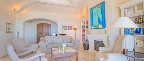 Uma sala de estar ampla com lareira, estante de livros e uma grande pintura abstrata.