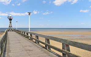 Une jetée en bois menant à une plage où se trouvent une tour de surveillance pour les sauveteurs et un lampadaire.