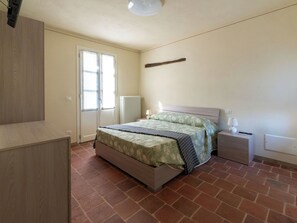 Ein Schlafzimmer mit einem Bett, einem Nachttisch, einem Heizkörper und einer Tür mit einem Fenster.