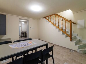 Ein Essbereich mit Tisch und Stühlen, eine Treppe mit Holzläufer und eine Deckenleuchte.