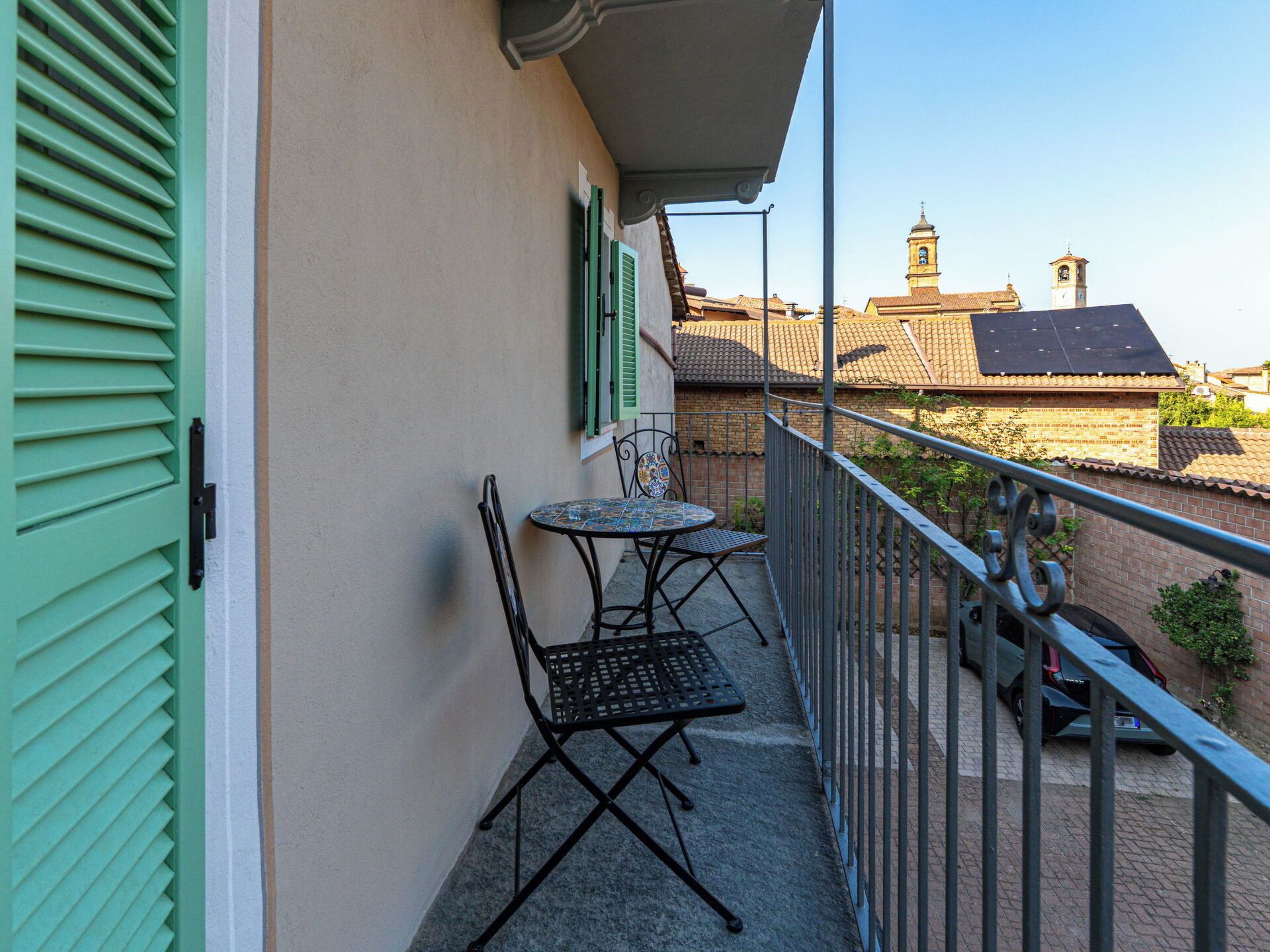 Un balcon avec une table et des chaises, une balustrade et une vue sur des immeubles et une tour en arrière-plan.