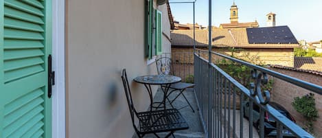 Un balcón con mesa y sillas, barandilla y vista a edificios y una torre al fondo.