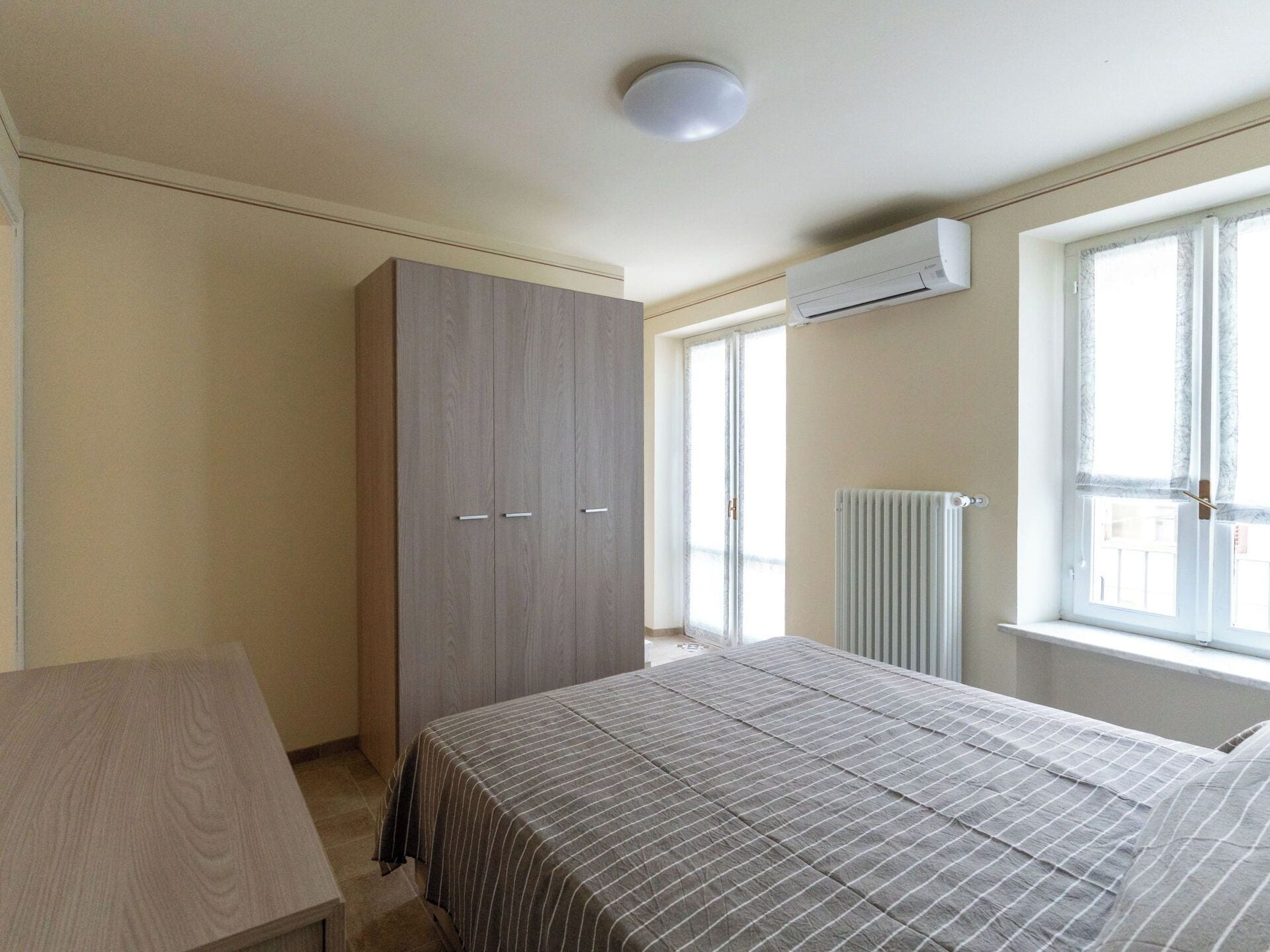 Une chambre à coucher avec un lit, une armoire, un radiateur et une fenêtre.