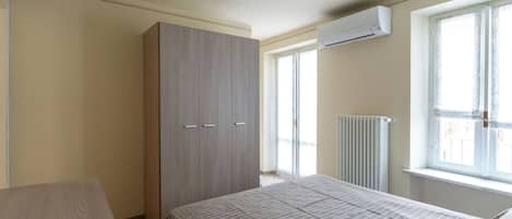 Un dormitorio con cama, armario, radiador y ventana.