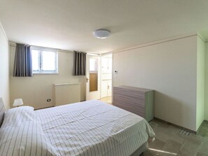 Ein Schlafzimmer mit einem Bett, einem Fenster mit Vorhängen, einem Heizkörper und einer Tür zu einem anderen Raum.