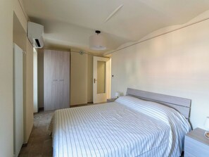 Quarto com cama, mesa de cabeceira, guarda-roupa e porta.