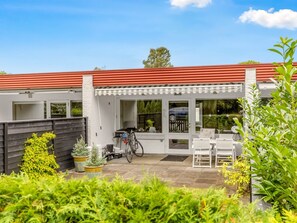 A modern house with a red roof, a covered patio with white furniture, and a bicycle parked outside.