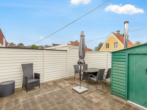 A patio area with a table and chairs, a covered umbrella, and a green shed.