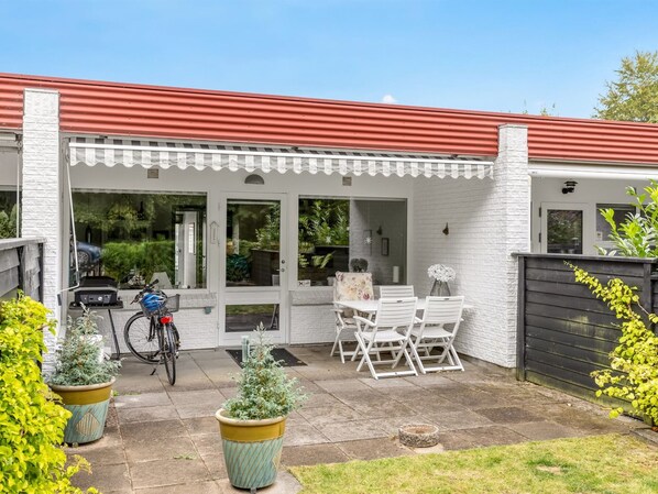 A covered patio with a table and chairs, a bicycle, and potted plants.