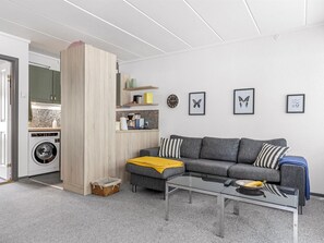 A modern living room with a grey sofa, a glass coffee table, and a kitchen area with a washing machine. - "Maureen" - 150m from the sea by Interhome (Haderslev)