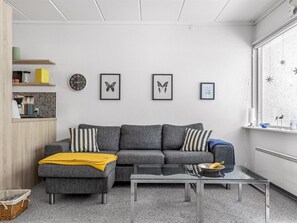 A modern living room with a grey sofa, striped pillows, a coffee table, and wall art including a clock and butterfly prints.