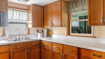 A kitchen with wooden cabinets, a white countertop, a sink, and a window with a patterned curtain.