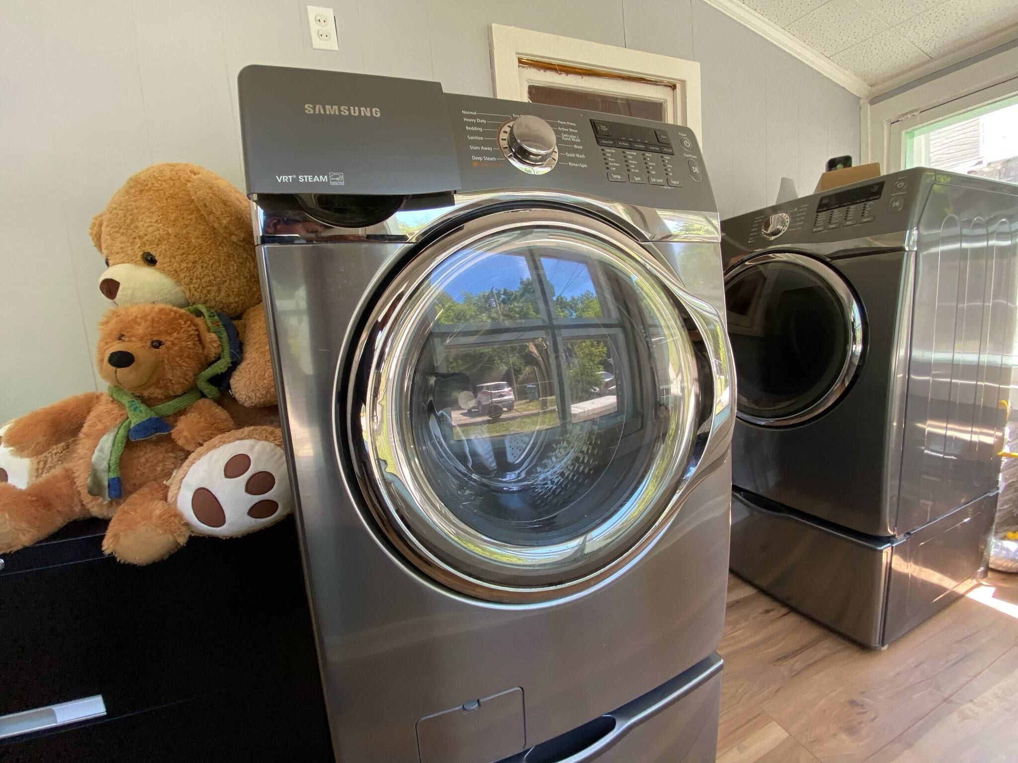 A Samsung VRT steam washer and dryer in a room with a teddy bear on the washer.