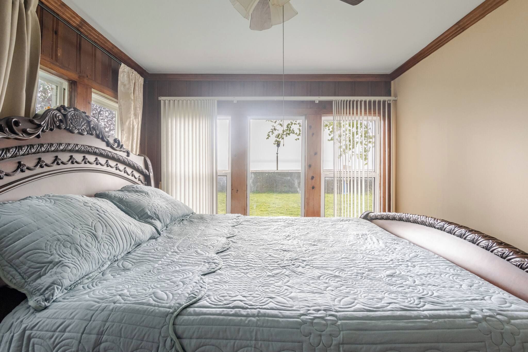 Un dormitorio con una cama grande, cabecero de madera y vistas a un jardín a través de un ventanal corredero.