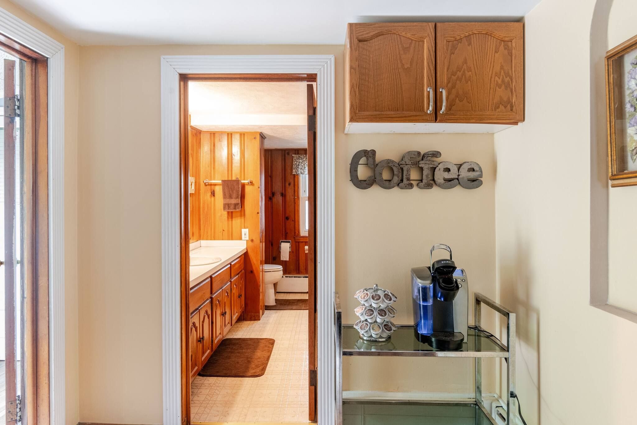 A hallway leading to a bathroom with wooden cabinets and a coffee sign.