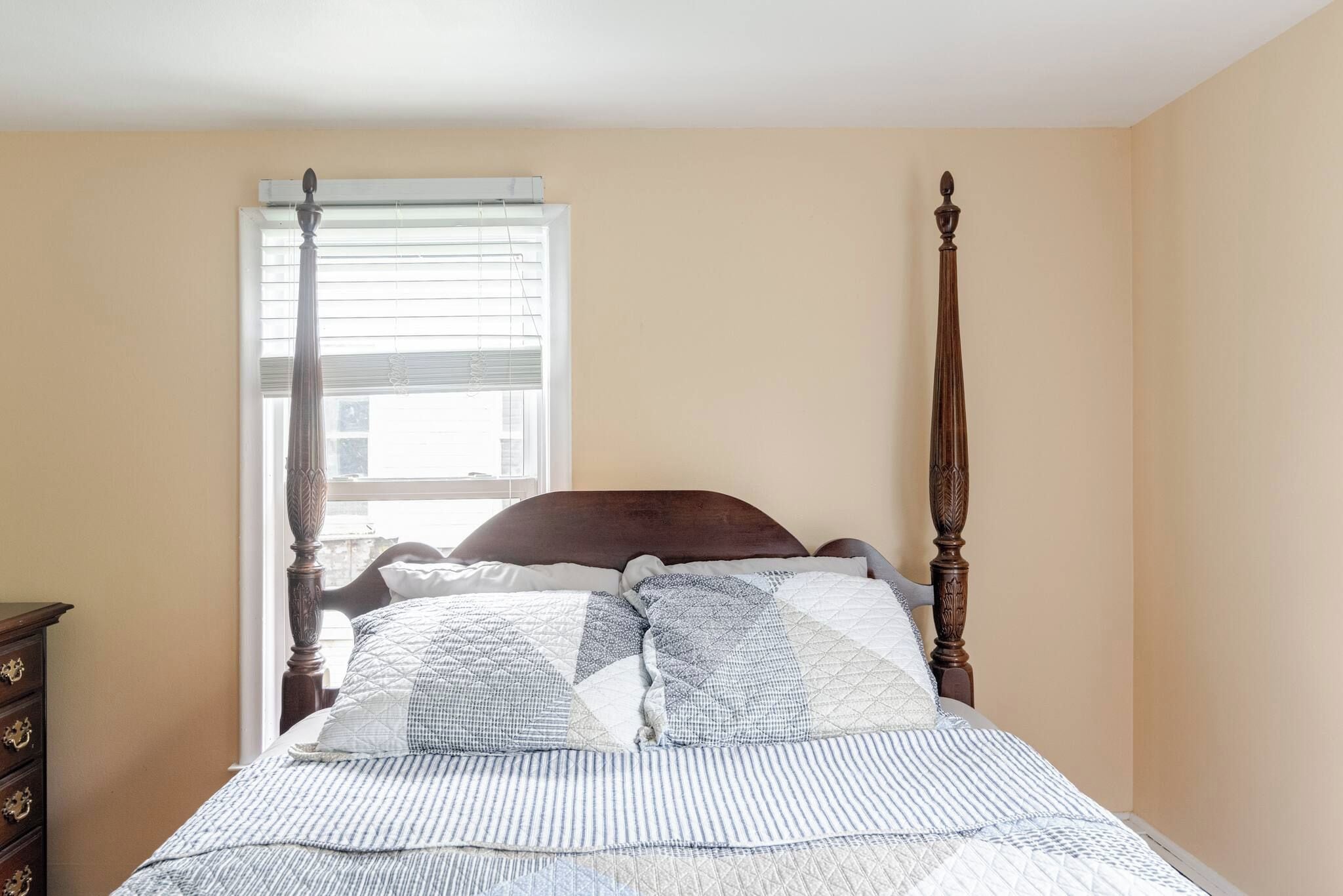 A bedroom with a four-poster bed, a window with blinds, and a dresser with drawers.
