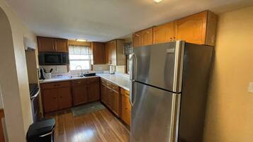 A compact kitchen with wooden cabinets, a stainless steel refrigerator, a microwave, and a window with patterned curtains.